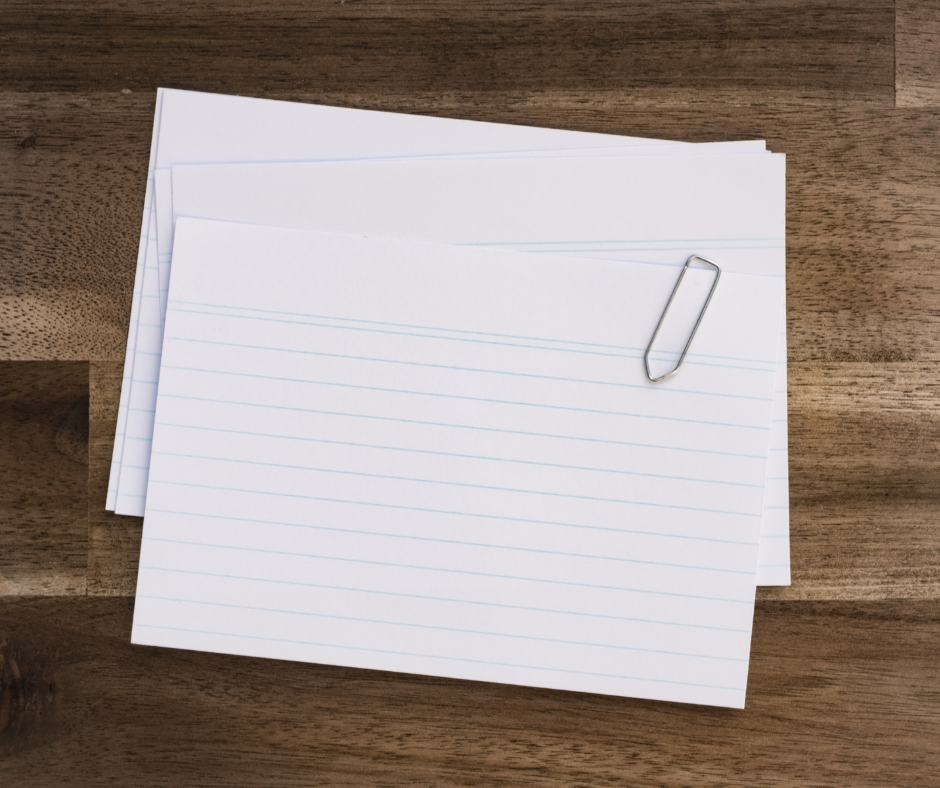 A stack of lined index cards held together by a paperclip on a wooden surface.