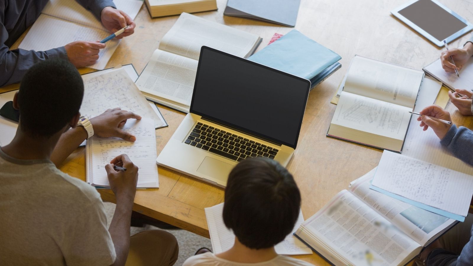 Group of people studying around a table with a laptop and open books.