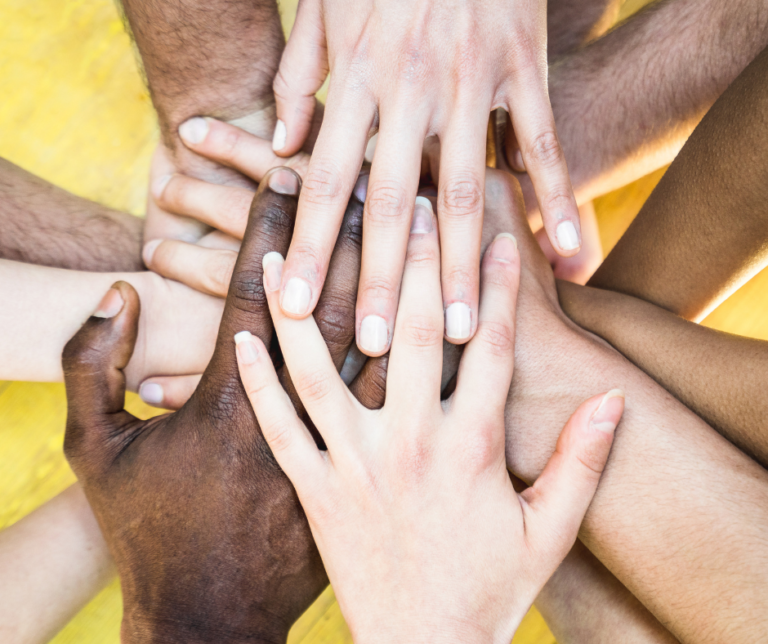 A diverse group of hands layered on top of each other in a symbol of unity and teamwork, set against a yellow background.