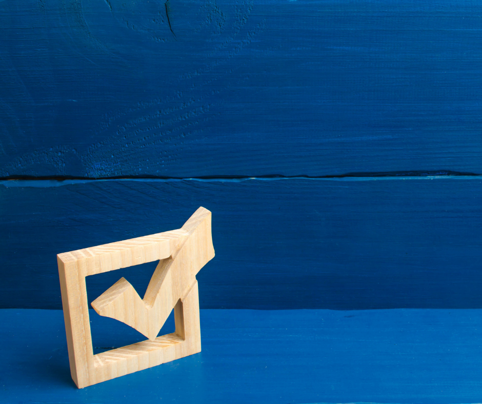 A wooden checkmark sculpture against a blue wooden background.