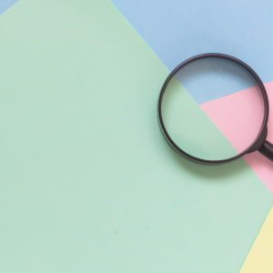 A black magnifying glass rests on a pastel-colored paper background with shades of blue, green, pink, and yellow.