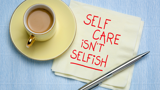 A cup of coffee with a pen and a napkin on which "SELF CARE ISN'T SELFISH" is written in red ink.