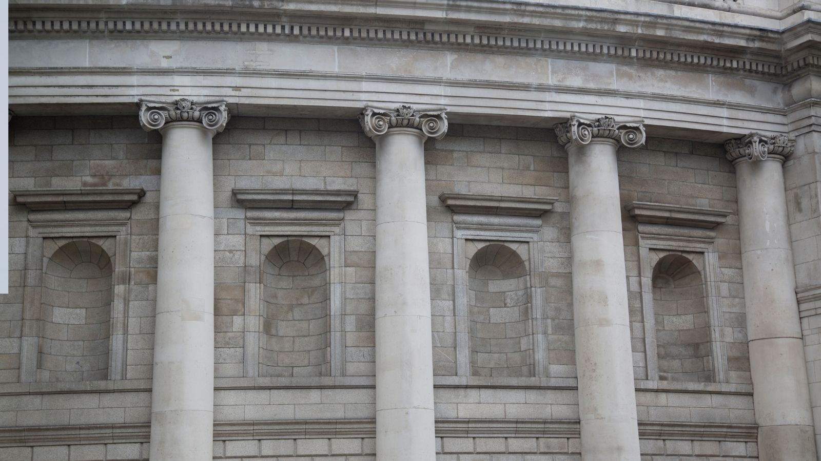 Close-up of a classical building facade with five Corinthian columns and sculpted arches between them.